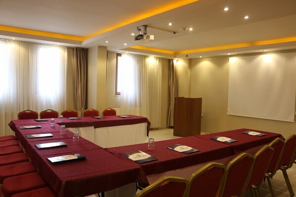 A conference room with a long table, red chairs, a podium, and a projector screen. - Akbak Otel (Ilgaz)