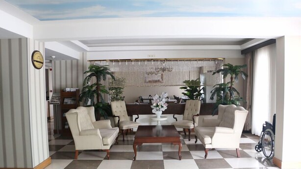 Un vestíbulo amplio con suelo a cuadros, una mesa de centro y cuatro sillones. Hay plantas en macetas y un candelabro.