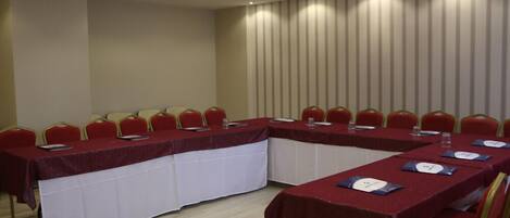 Un salón de conferencias con una larga mesa, sillas rojas y un proyector en el techo.