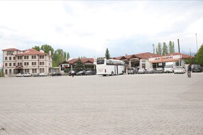 A parking lot with a white bus, several cars, and buildings with signs "AKOMEK" and "OTEL".