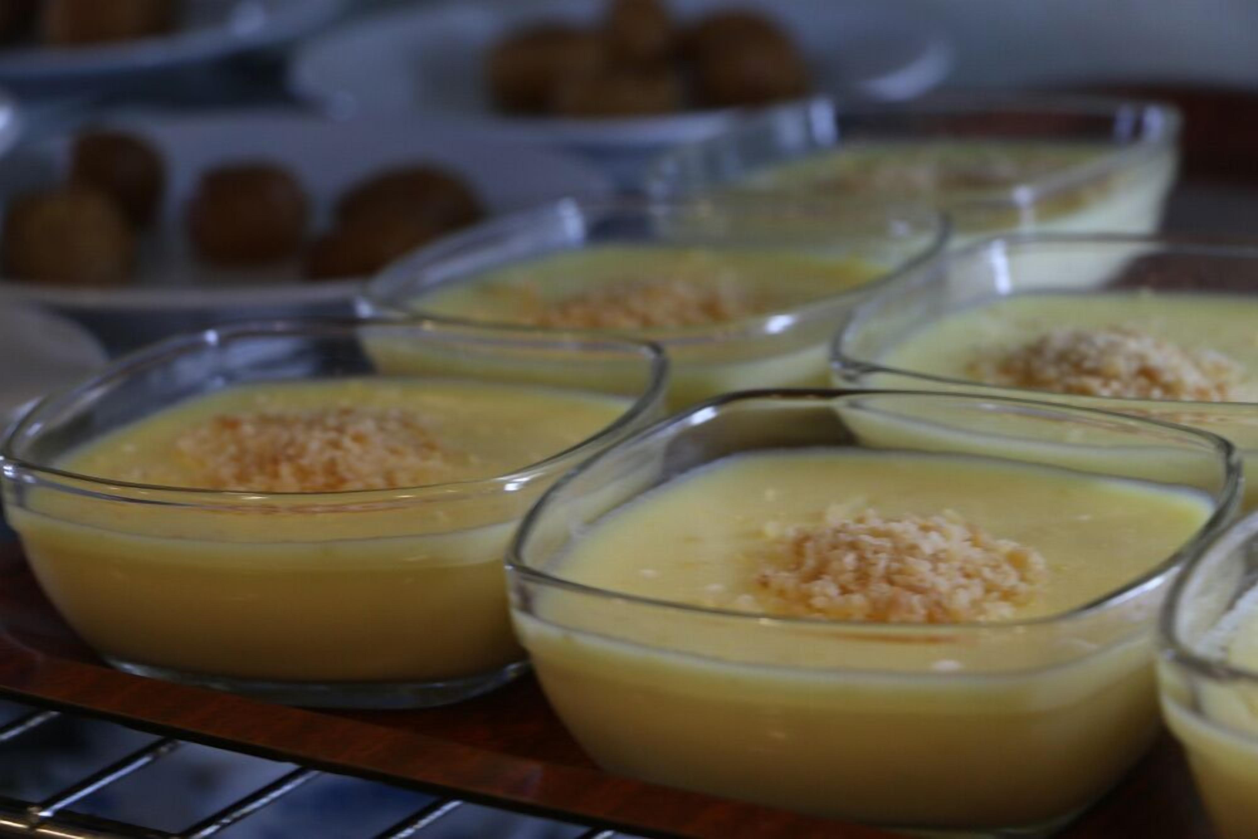 Una bandeja de postres con crema pastelera amarilla servida en pequeños recipientes de vidrio, adornada con una cobertura desmenuzable.