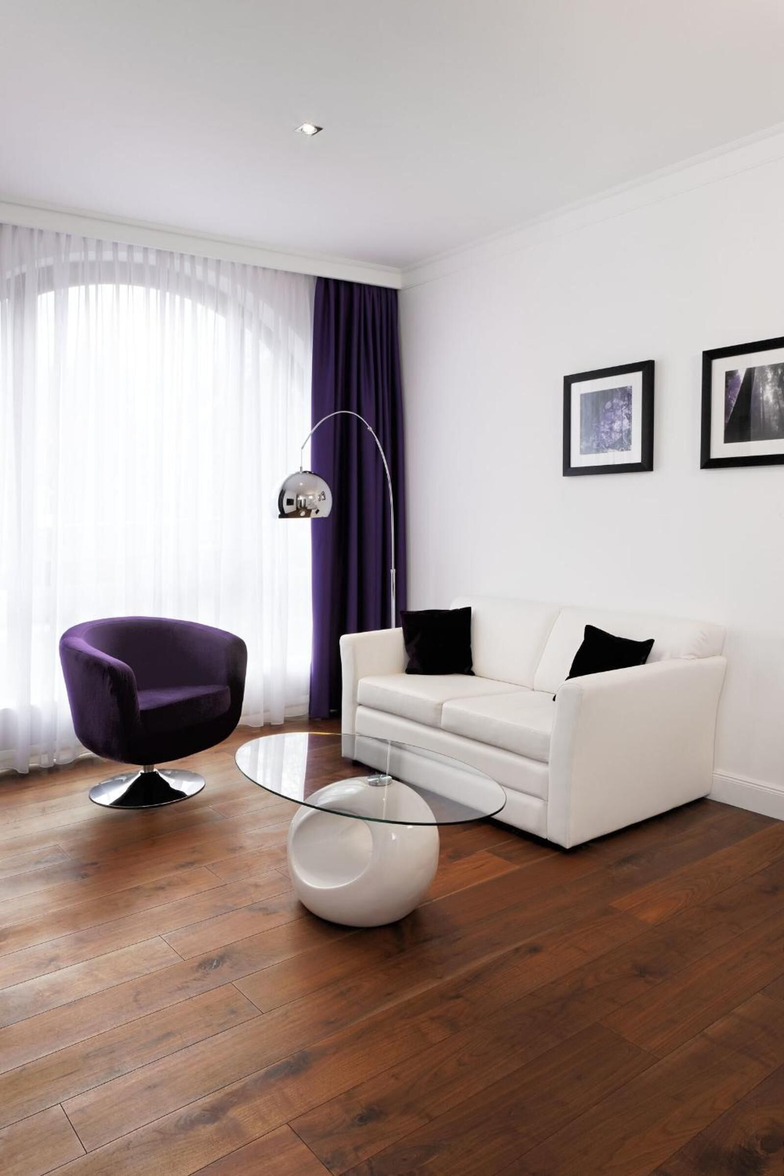 A modern living room with a white sofa, a purple armchair, a glass coffee table, and a floor lamp.