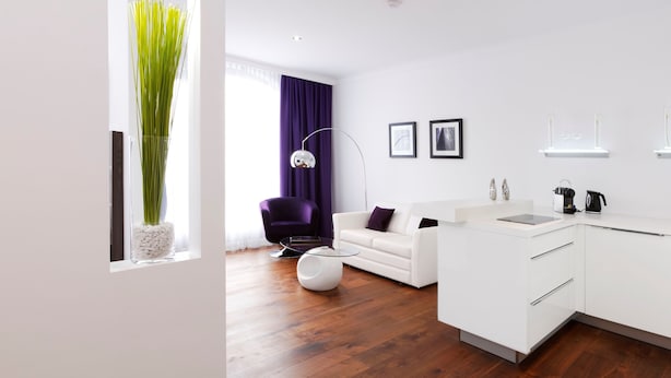 Un salon moderne avec un canapé blanc, une table basse en verre et un fauteuil violet.