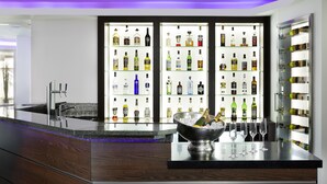 Un espace bar moderne, avec un assortiment de bouteilles d’alcool, un comptoir et un grand récipient rempli de verres et de bouteilles.