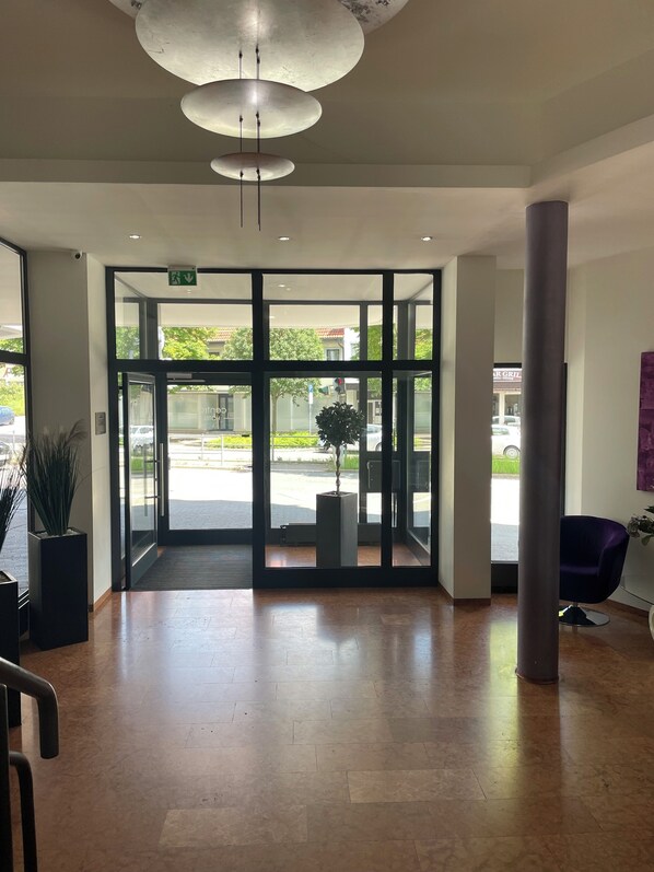 A spacious lobby with a modern design, featuring a large glass door entrance, a potted plant, and a seating area with a purple chair.