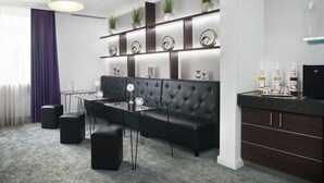 Un salon moderne avec un canapé noir, une table basse en verre et un coin repas comprenant une table et des chaises noires. Des objets décoratifs sont disposés sur les étagères, et il y a également un coin cuisine avec un plan de travail et des placards de couleur sombre.