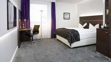 A hotel room with a bed, desk, chair, and a wardrobe.