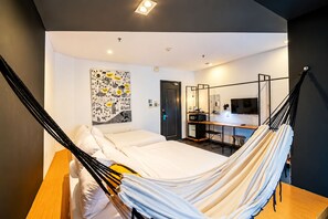 Habitación de hotel moderna con cama, escritorio, silla, televisor y una hamaca.