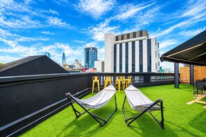 A rooftop terrace with artificial grass, two hammocks, and yellow chairs. - The Hammock Hotel Ben Thanh (Ho Chi Minh City)