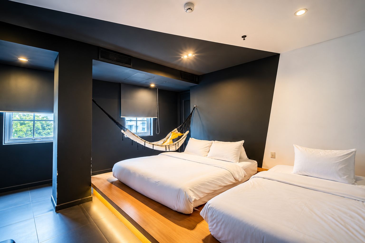 Quarto moderno com duas camas, uma rede e janela que proporciona iluminação natural.