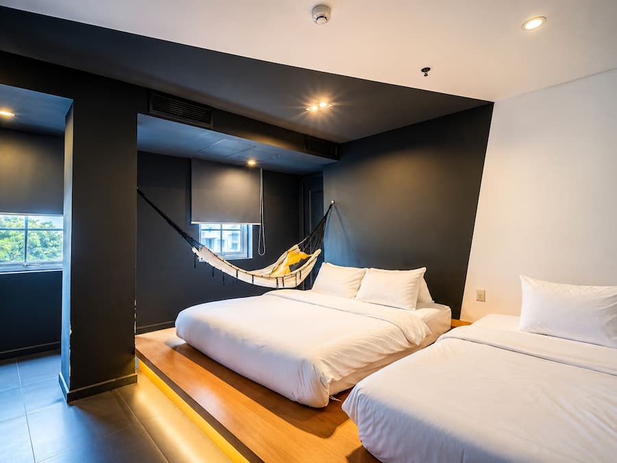 A modern bedroom with two beds, a hammock, and a window providing natural light.