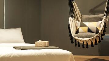 A modern bedroom with a bed, a hanging chair, and a small gift on the bed.