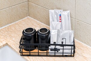 A bathroom corner with a marble countertop, a black metal rack holding two black bottles and several white toiletry bags.