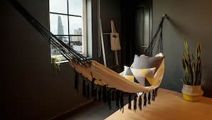 Una silla hamaca con vistas a un paisaje urbano a través de una ventana, una planta en maceta y un cuadro en la pared.