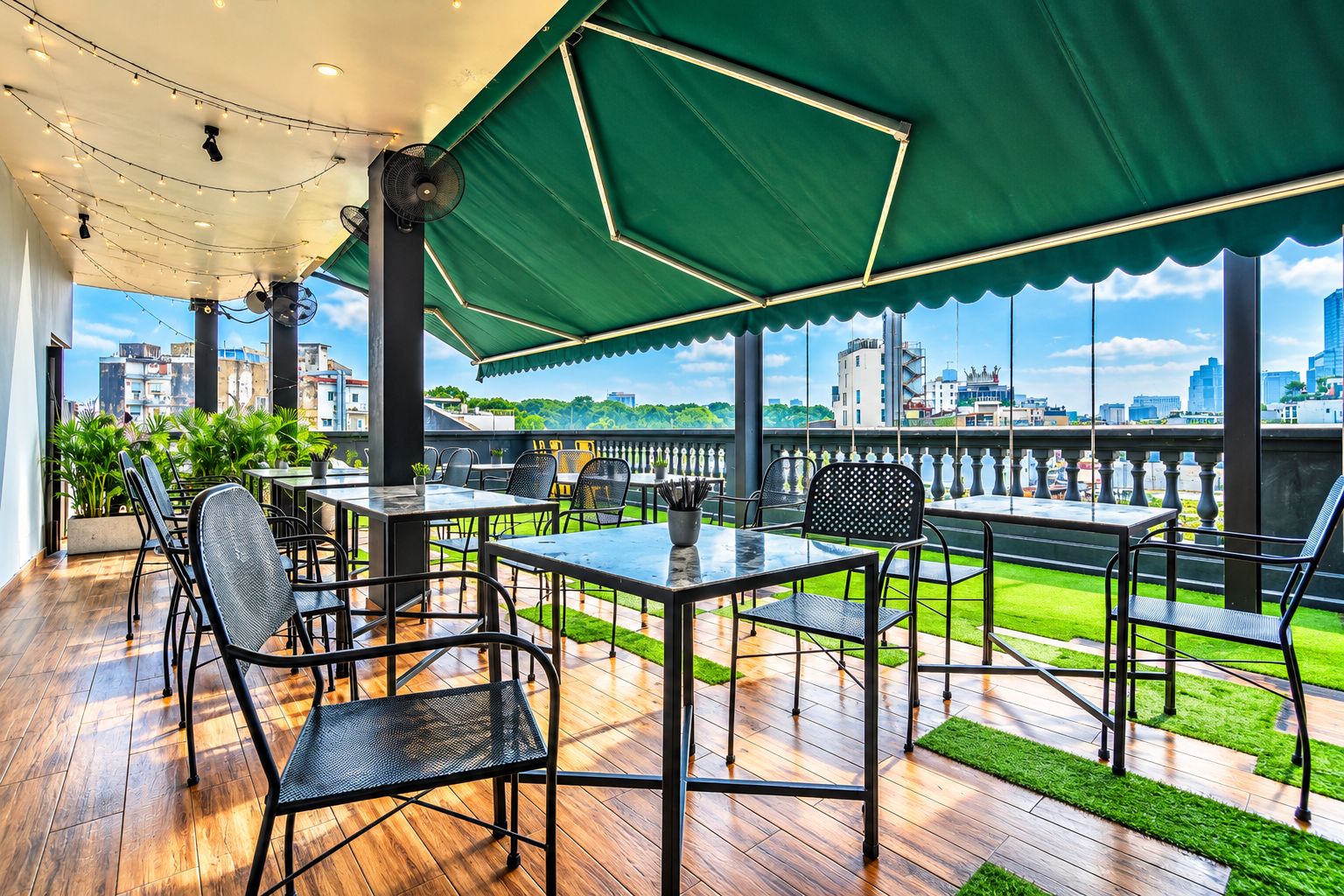 An outdoor terrace with tables and chairs, a green canopy, and a city view.