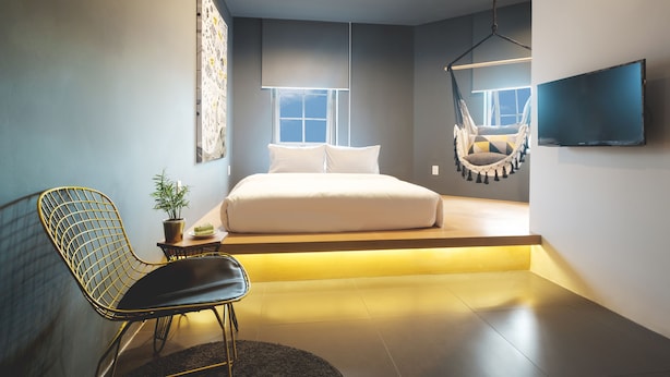 Un dormitorio moderno con una cama, una silla colgante, un televisor y una ventana.