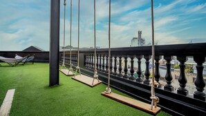 Terraza en la azotea con césped artificial, una hamaca y columpios, con vistas a un paisaje urbano.