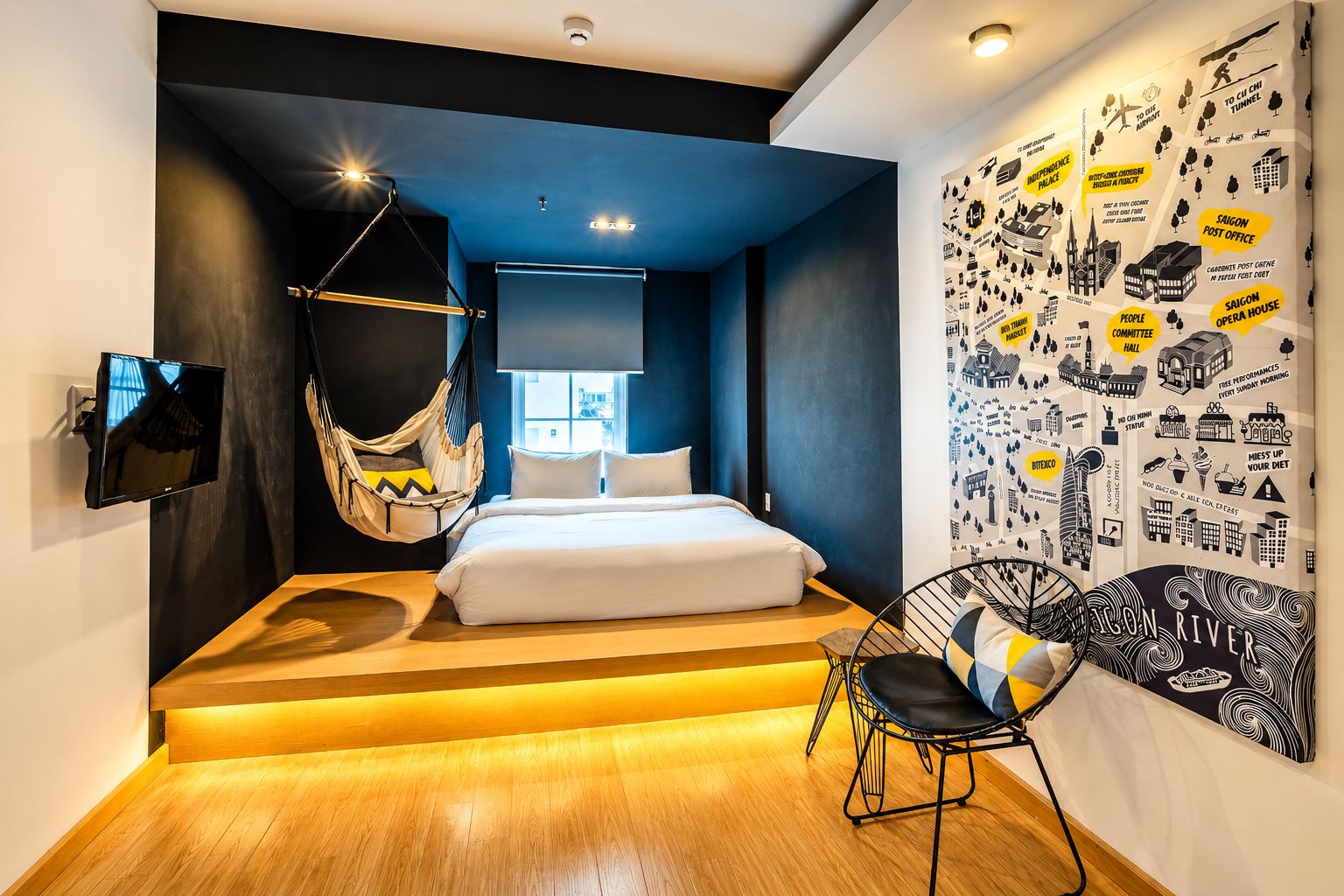 A modern bedroom with a bed, a hanging chair, a television, and a wall with various illustrations.