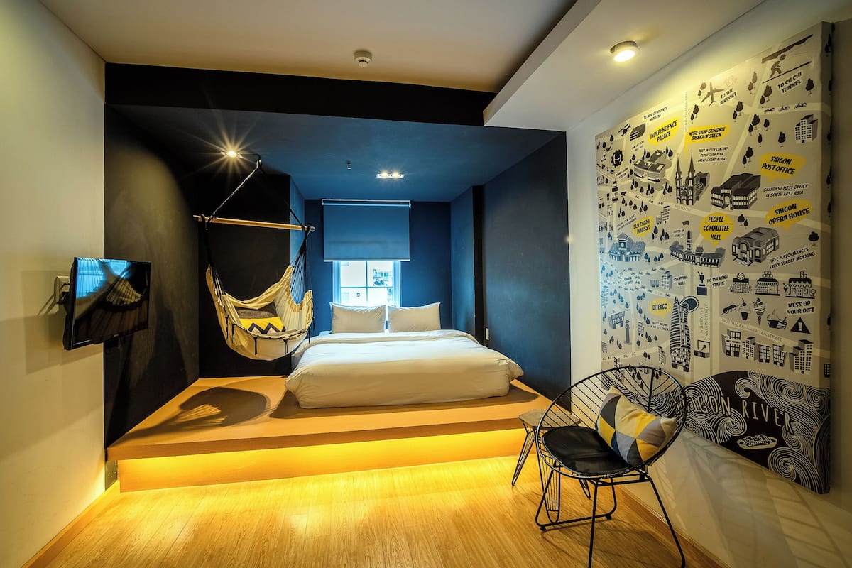 Une chambre moderne avec un lit, un fauteuil suspendu, un canapé et un mur décoré d’illustrations représentant un paysage urbain.