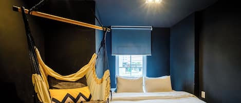 A room with a bed, a hanging chair, and a window with blinds.