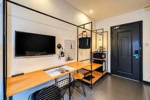 A modern hotel room with a flat-screen TV, a wooden desk, a chair, a coat rack, a grid wall organizer, and a door with a keycard lock. - The Hammock Hotel Ben Thanh (Ho Chi Minh City)