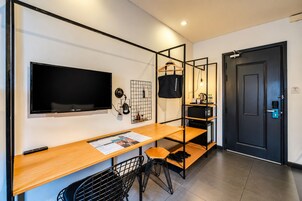 Una habitación de hotel moderna con una televisión de pantalla plana, un escritorio de madera, una silla, un perchero, un organizador de pared tipo rejilla y una puerta con cerradura de llave electrónica.