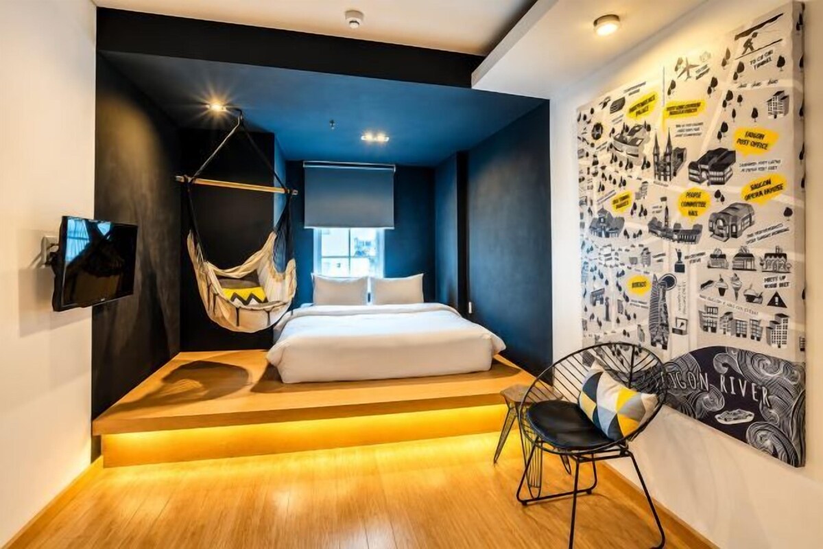 A modern bedroom with a hanging chair, a bed, and a wall with travel-themed artwork.
