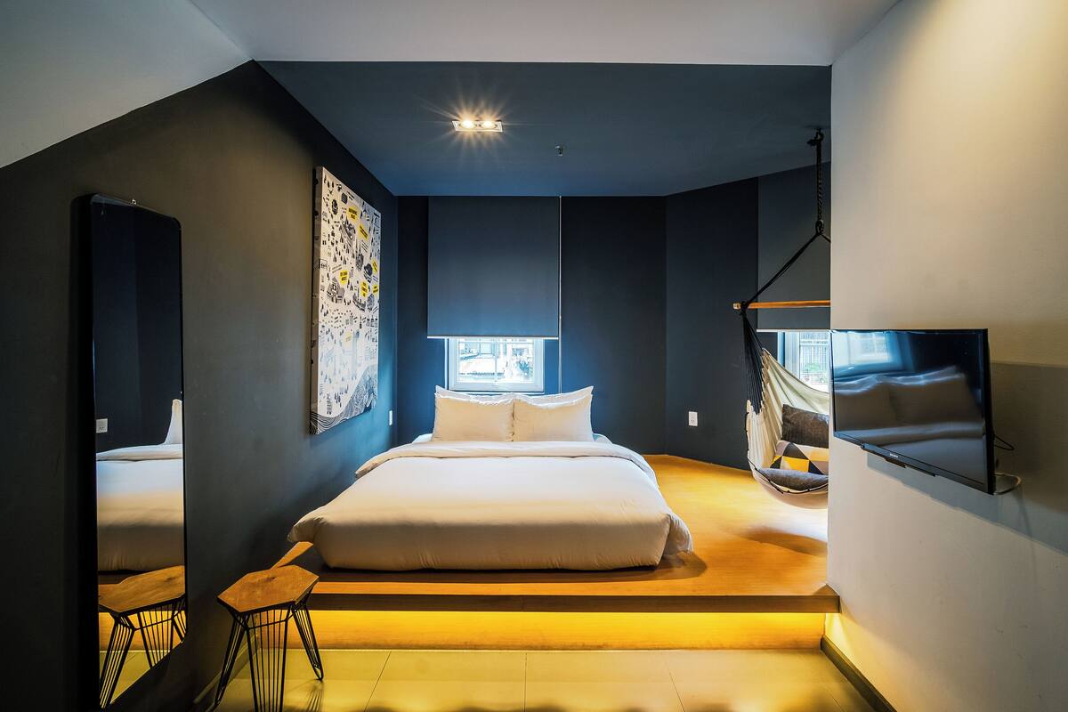 Une chambre moderne avec un grand lit, un hamac et un téléviseur fixé au mur.
