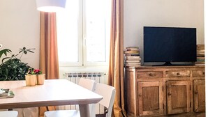 A dining area with a table, chairs, a hanging light fixture, a radiator, and a television on a wooden cabinet. - Panoramic Castle Apartment, Trastevere, Old Town, Free Parking (Roma)
