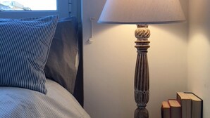 A bedside table with a lamp, a striped pillow, and a stack of books. - Panoramic Castle Apartment, Trastevere, Old Town, Free Parking (Roma)