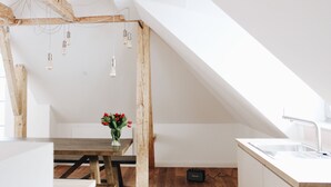 Una cocina moderna con una mesa de madera, un jarrón de flores rojas y una encimera blanca con un lavamanos.