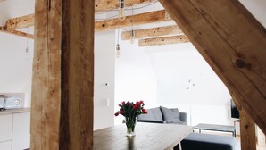 Una mesa de comedor de madera con un jarrón de flores rojas, una zona de cocina con un radio y un espacio de estar con sofá y televisor.