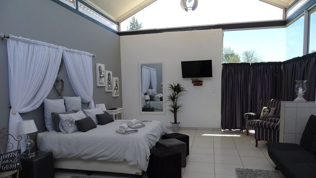 A modern bedroom with a large bed, bedside tables, a TV, and a seating area with a sofa and armchair. - Eden Self Catering Chalets (Windhoek)