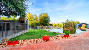 A paved pathway with a stone wall on one side and a pond with a small bridge in the center. - Eden Self Catering Chalets (Windhoek)