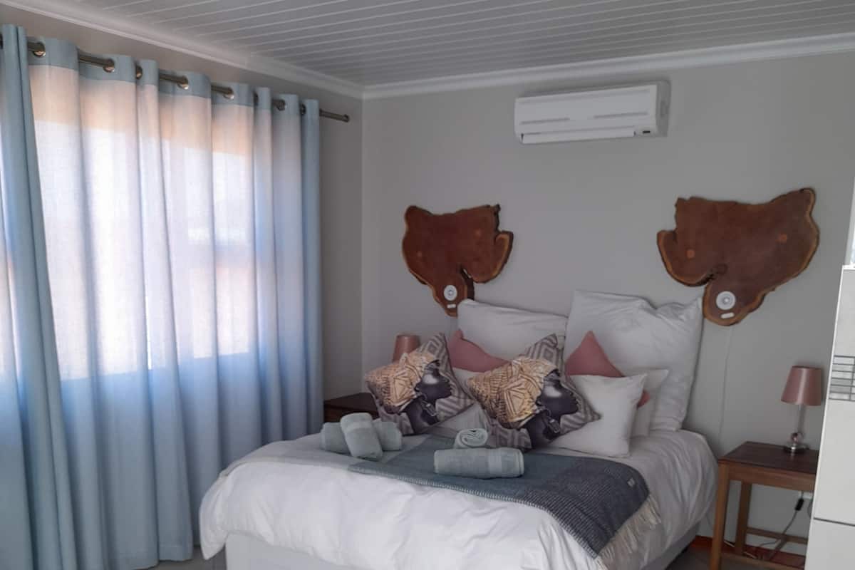 A bedroom with a bed, curtains, a rug, a bedside table, and wall decor.