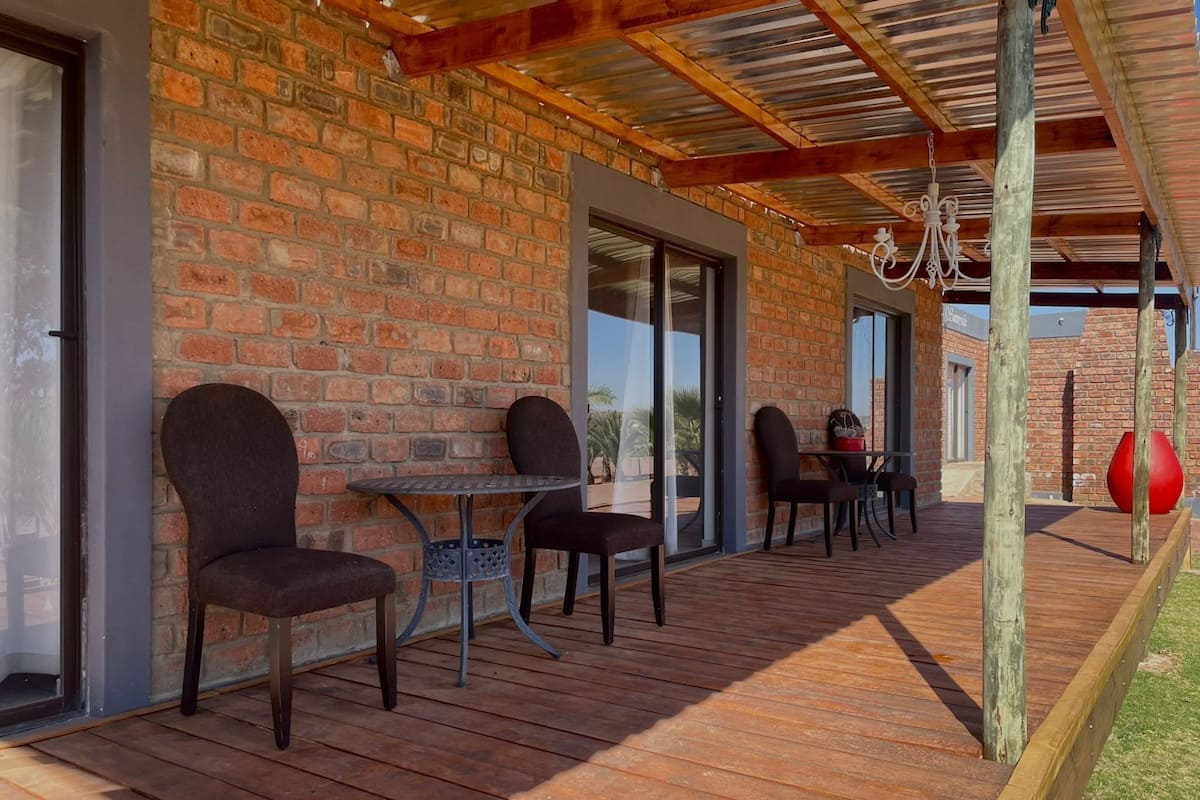 An outdoor patio with brick walls, wooden flooring, and metal tables and chairs.