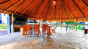 An outdoor covered patio with stone flooring, wooden chairs, a table, and a Coca-Cola refrigerator. - Eden Self Catering Chalets (Windhoek)