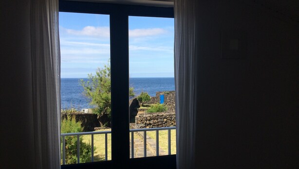 Una habitación con vista al mar a través de una ventana con cortinas.