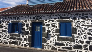 Un edificio de piedra con puerta y contraventanas azules, techo de tejas y chimenea.