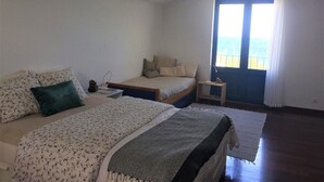 Un dormitorio con una cama, una cama individual, una mesita de noche, una lámpara y vistas al mar a través de una ventana.