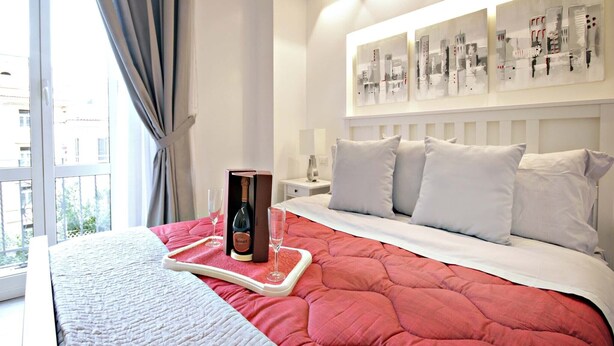 A hotel room with a large bed, a nightstand, a window with curtains, and artwork on the wall. - NEW Velvet Trastevere Apartment (Roma)