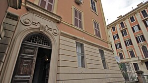 A building with a large wooden door, multiple windows with shutters, and a balcony with a metal railing. - NEW Velvet Trastevere Apartment (Roma)