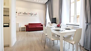 A modern living room with a red sofa, a dining table set for four, and a TV on a stand. - NEW Velvet Trastevere Apartment (Roma)