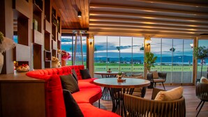 A modern lounge area with a red sofa, round tables, and chairs, overlooking a scenic view. - Paradiso Hotel (Nessebar)