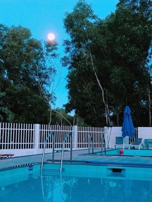Una piscina con valla blanca, árboles y una sombrilla azul.
