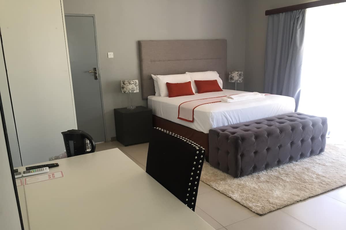A neatly arranged bedroom with a bed, bedside tables, a desk, and a large ottoman.