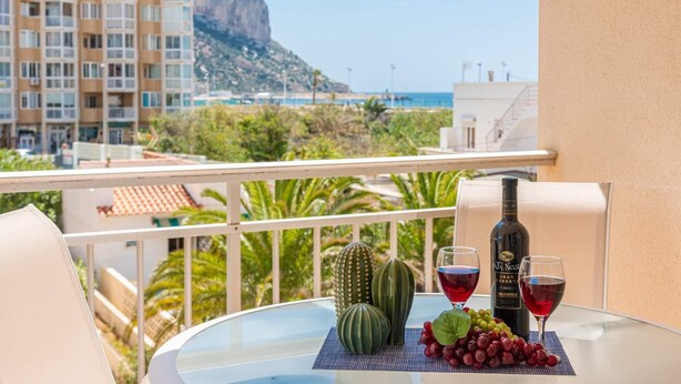 Un balcón con una mesa dispuesta para una comida, una botella de vino y una copa de vino tinto.
