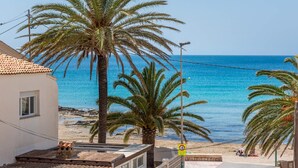 Vista costera con playa, palmeras y un edificio con techo de tejas.