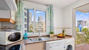 Cocina compacta equipada con microondas, estufa, pileta y lavadora. Una ventana ofrece vistas a edificios altos.