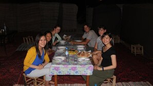 A group of people seated around a table with a floral tablecloth, in a room with patterned carpet and wooden furniture. - Galaxy Desert Camp Merzouga (Taouz)